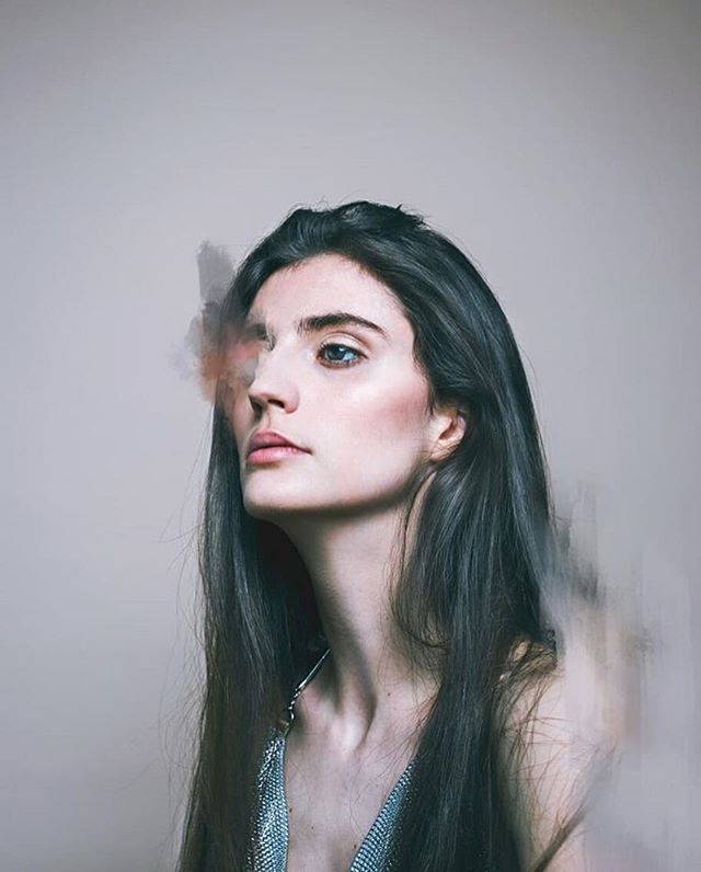 A contemplative woman with long dark hair looks off-camera in a soft, dreamy portrait.