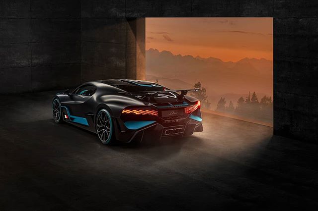 A black Bugatti Divo with blue accents sits against a sunset backdrop, showcasing luxury and performance.