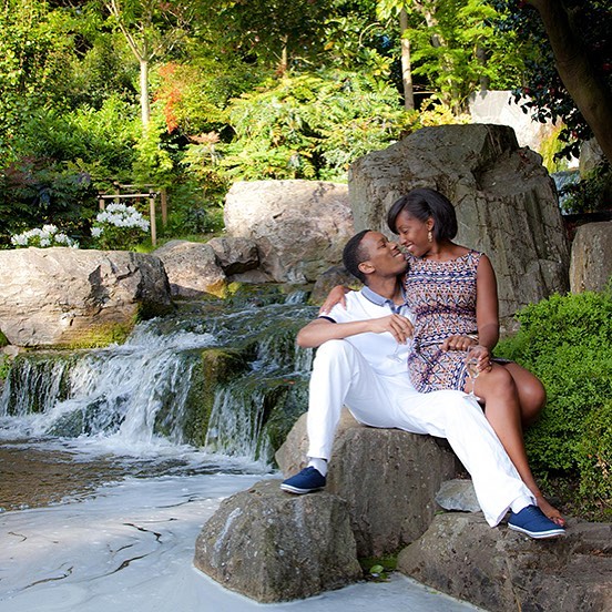 A loving couple share a tender moment by a scenic waterfall in a lush garden setting.