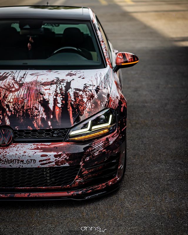 A menacing VW GTI with a custom blood-splatter paint job stands out on the asphalt.