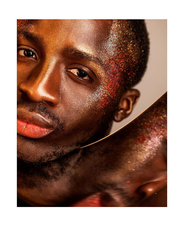 An attractive African American man with glitter on his face posing in a studio for a beauty or skincare ad.