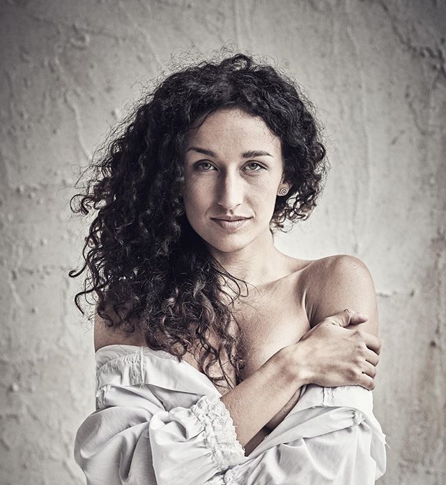 Portrait of a brunette woman with curly hair looking at the camera in soft light.