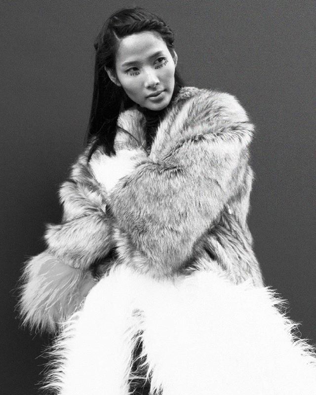 An asian model poses wearing a luxurious fur coat in a stylish black and white editorial fashion shot.