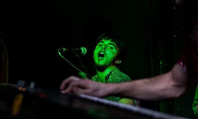 A man intensely sings and plays the keyboard on stage during a vibrant live music performance.