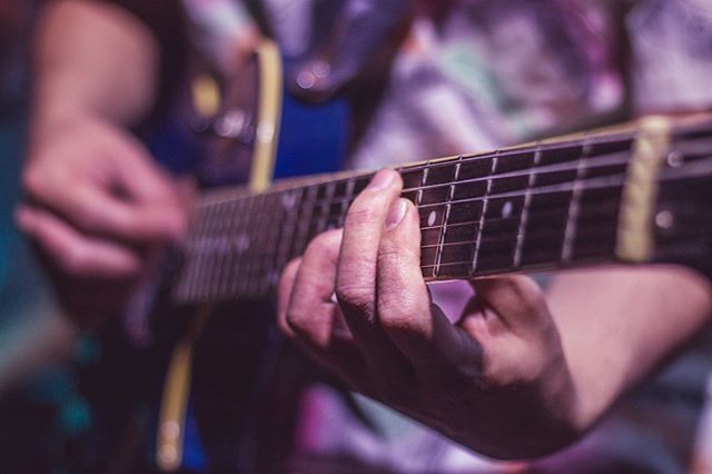 Close-up of a person playing an electric guitar, focusing on their hands on the fretboard in warm, muted light.