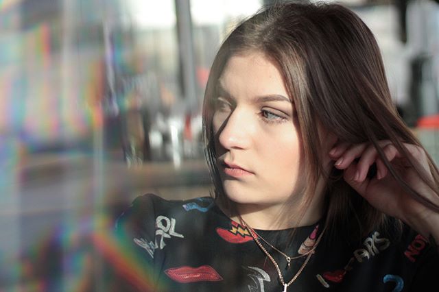 A young woman gazes thoughtfully in soft, natural light, creating a moody and intimate portrait.