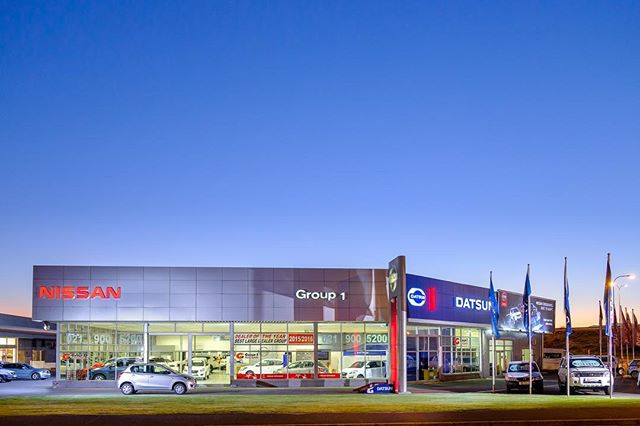 A modern car dealership with Nissan and Datsun brands, capturing a commercial scene in a city setting during daylight.