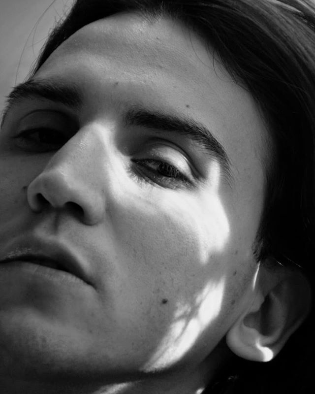 A close-up, black and white portrait of a man's face in soft, natural lighting, showcasing a minimalist and contemplative style.