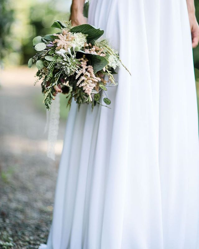 A bride in a white gown holds a delicate bouquet in a dreamy outdoor wedding setting. 