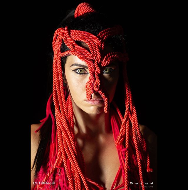 A striking portrait of a woman with artistic red rope headwear on a dark background.