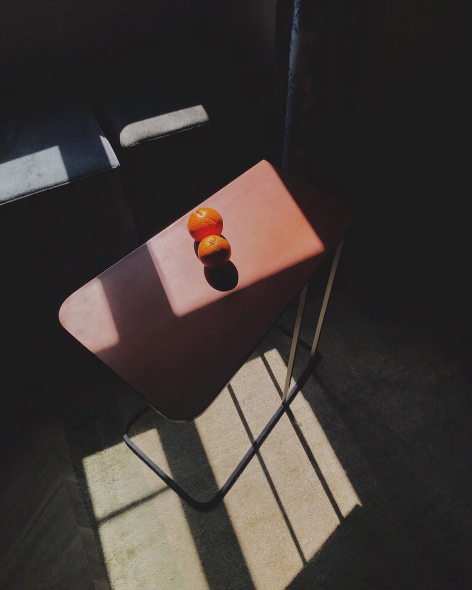 Two tangerines sit on a table bathed in sunlight, creating a minimalist and inviting still life.