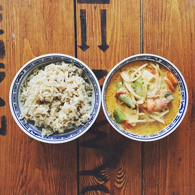 Overhead shot of two bowls, one with rice and one with curry, presented on a wooden surface.