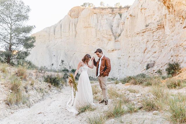 A couple tenderly hold hands amidst a beautiful desert landscape, perfect for wedding content.