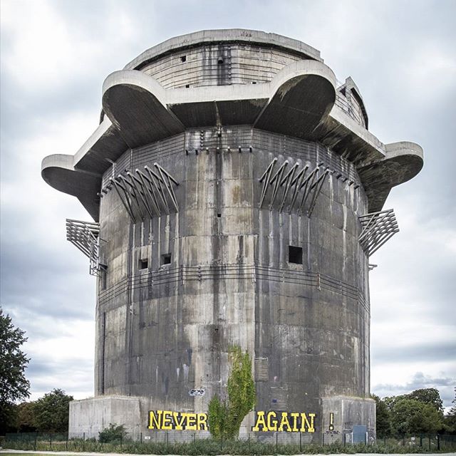 A historical flak tower with a powerful message 'Never Again' spray-painted on its base, standing as a reminder.