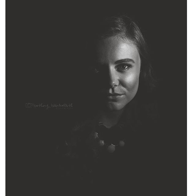 A black and white portrait of a woman with soft lighting and a dark, minimalist background.