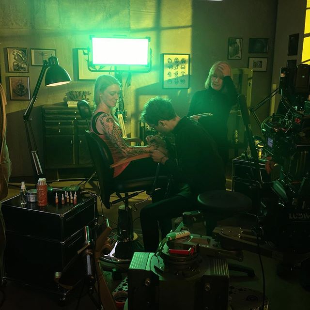 A woman gets a tattoo in a vintage-style studio, with a tattoo artist focused on their work.
