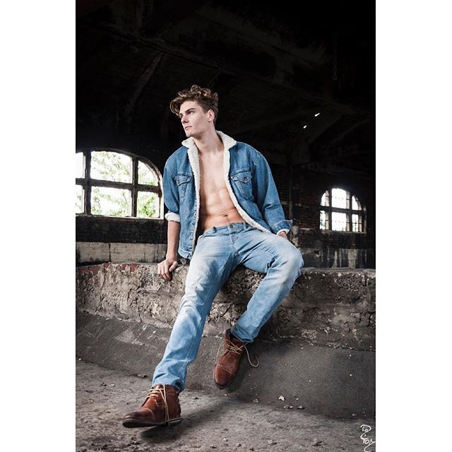 A stylish man poses in a denim jacket and jeans in an abandoned building, fashion editorial.