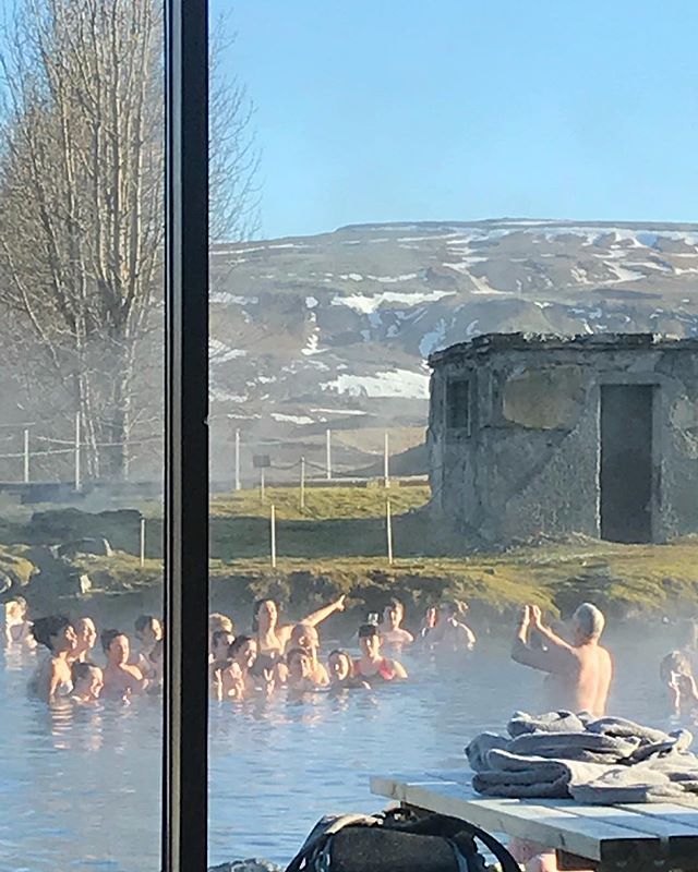 People enjoying a sunny day swimming in a geothermal hot spring with mountains in the background in Iceland.
