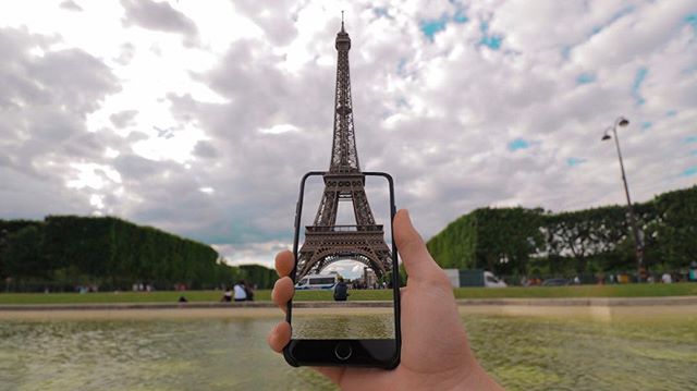 A hand holds a cellphone framing the Eiffel Tower in Paris, creating a picturesque scene.