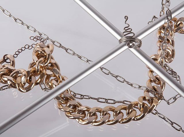 A close-up shows gold and silver chains intertwined through a metal frame creating a display of luxury and modern style.
