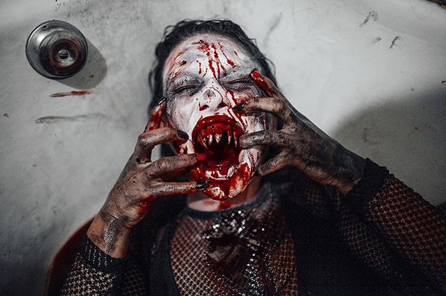A scary vampire woman with bloody face, long teeth, and dark eyes stares intensely, creating a spooky Halloween themed image.