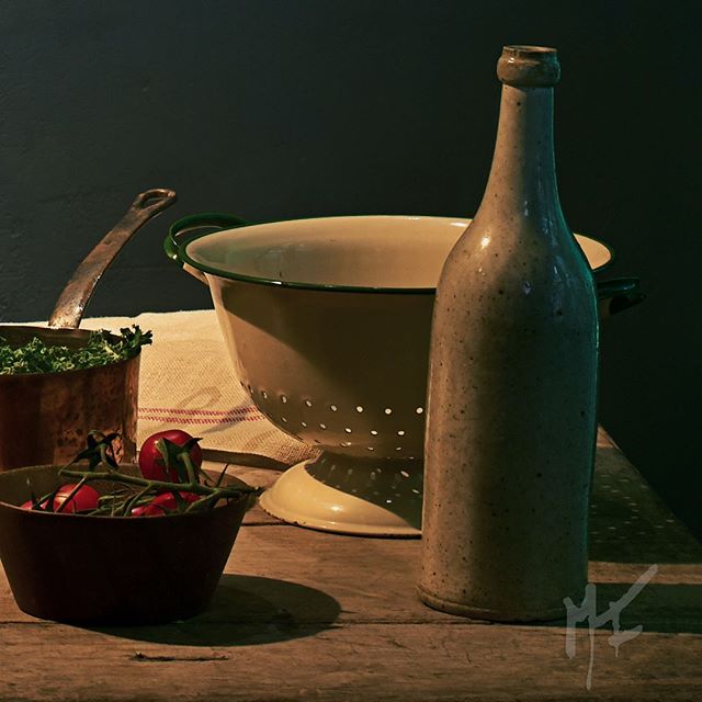 A vintage still life featuring a bottle, tomatoes, and kitchenware on a rustic table, perfect for culinary themes.