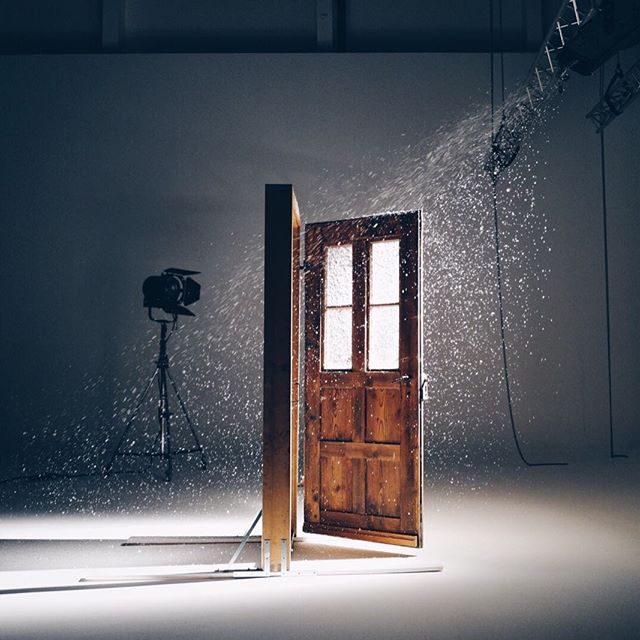 A wooden door stands open in a studio setting, backlit with light streaming through, creating a sense of mystery and invitation.