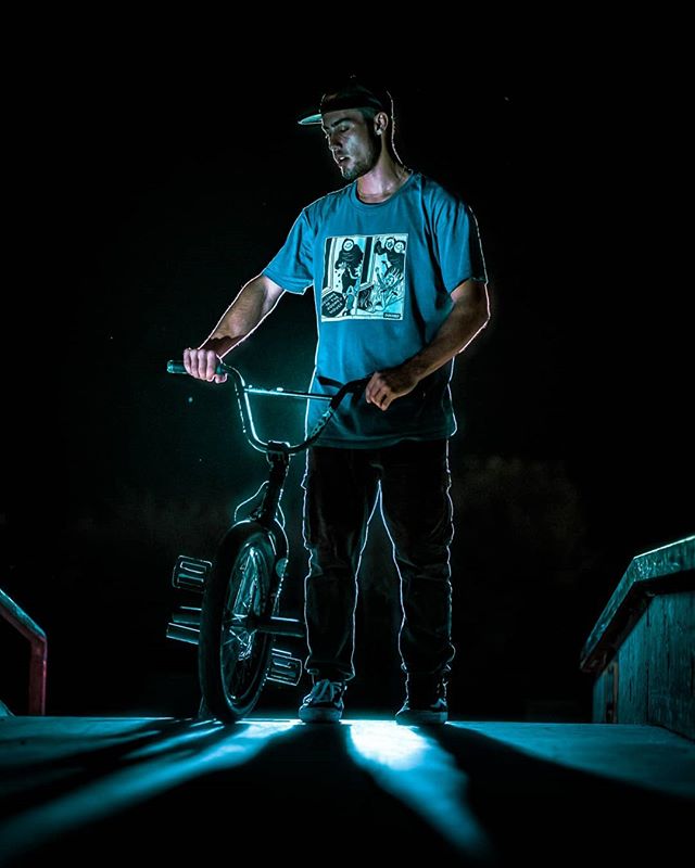 A man poses with his bmx bike at night with cool, contrasting, and directional lighting.