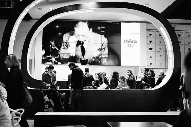 A monochrome shot of customers at a Lavazza coffee bar, waiting at the counter.