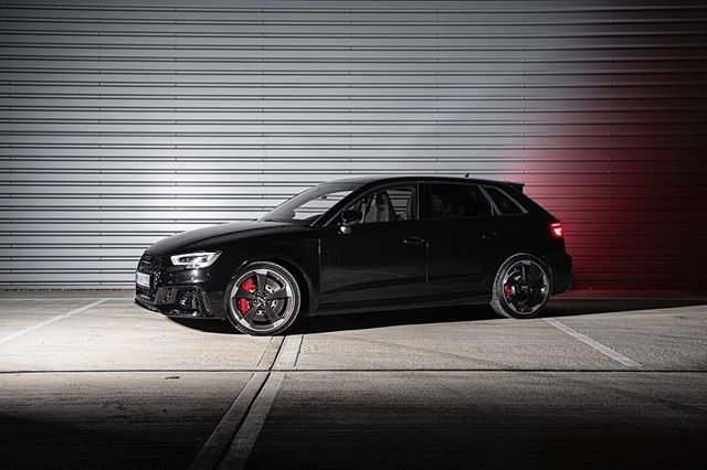A sleek black Audi RS3 hatchback is parked in a studio setting, showcasing its modern design.