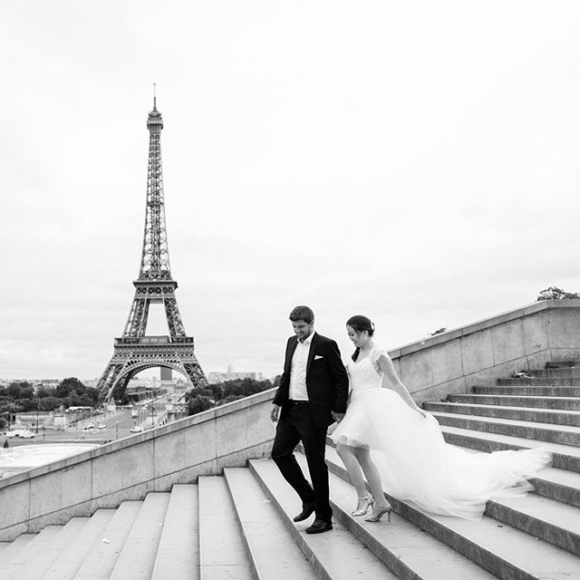 A bride and groom walk down the stairs with the Eiffel Tower in the background on their wedding day.