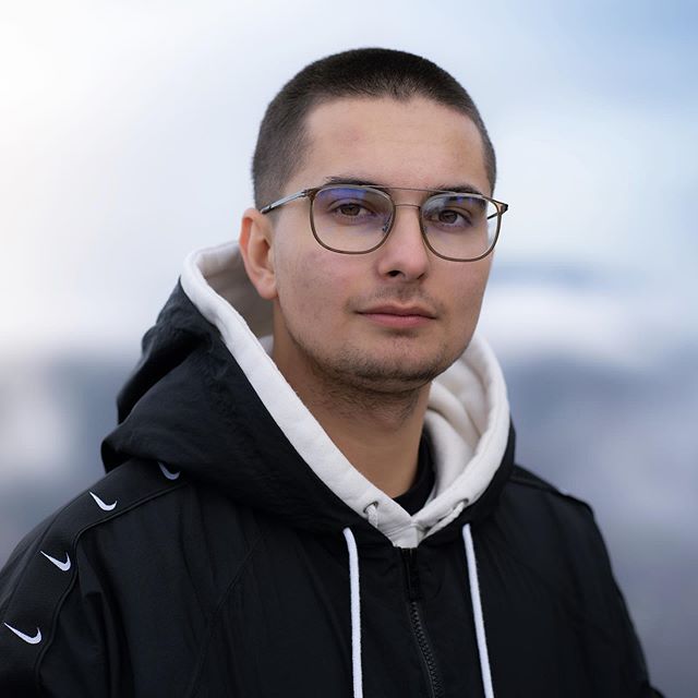 A man with glasses wearing a black and white Nike jacket poses outdoors.