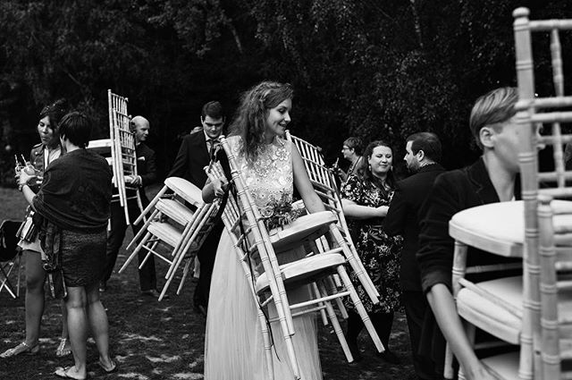 Wedding guests help set up chairs at an outdoor wedding event, in black and white.