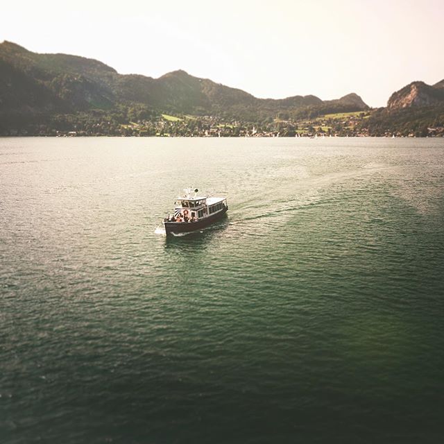 A boat sails on a serene lake surrounded by mountains under a clear sky. A scenic landscape shot for travel and tourism.