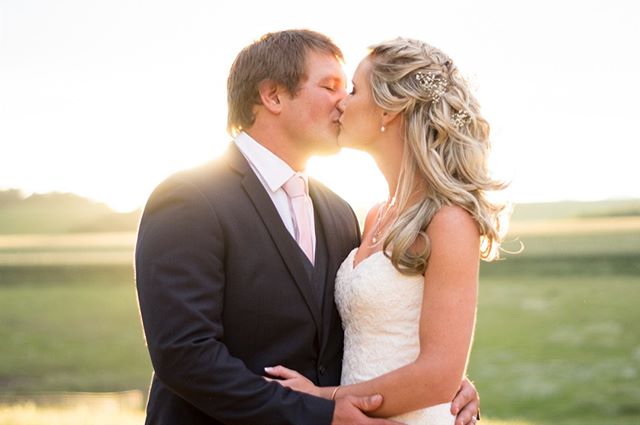 A bride and groom share a kiss outdoors, celebrating their wedding day in a romantic countryside setting.