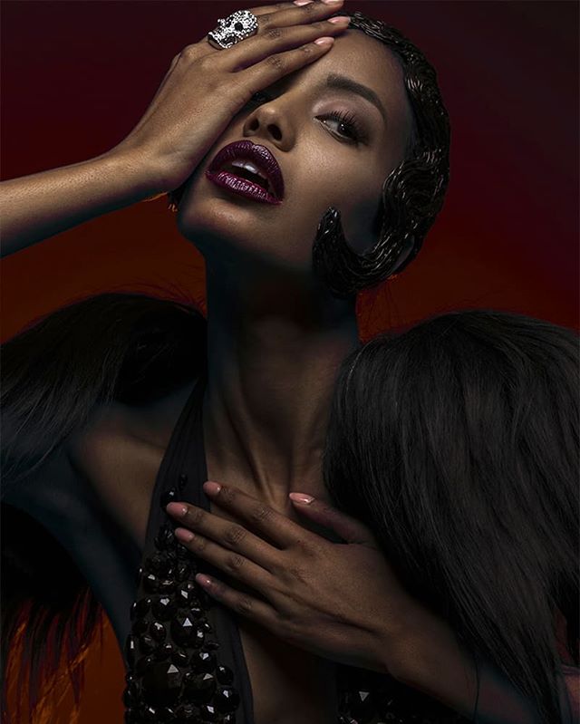 An elegant portrait showcases a woman with dark lips and a statement ring in a dramatic, editorial style.