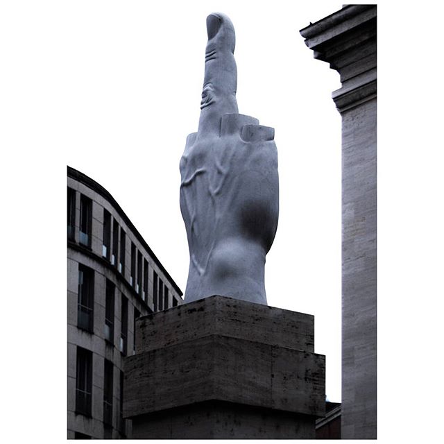 A large middle finger statue stands in an urban environment, capturing attention with its bold statement.