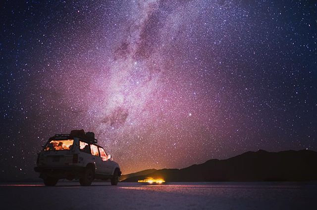 A vehicle sits under a stunning night sky filled with stars and the Milky Way in a serene desert landscape.