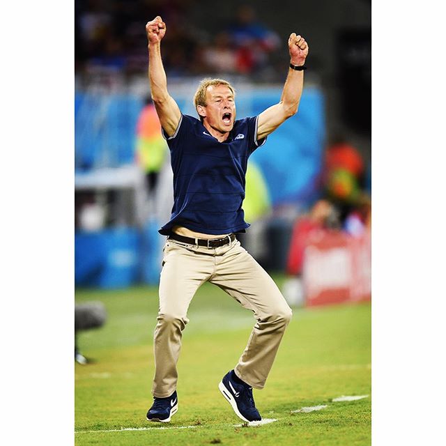 A coach celebrates a soccer victory with an excited jump on the field.