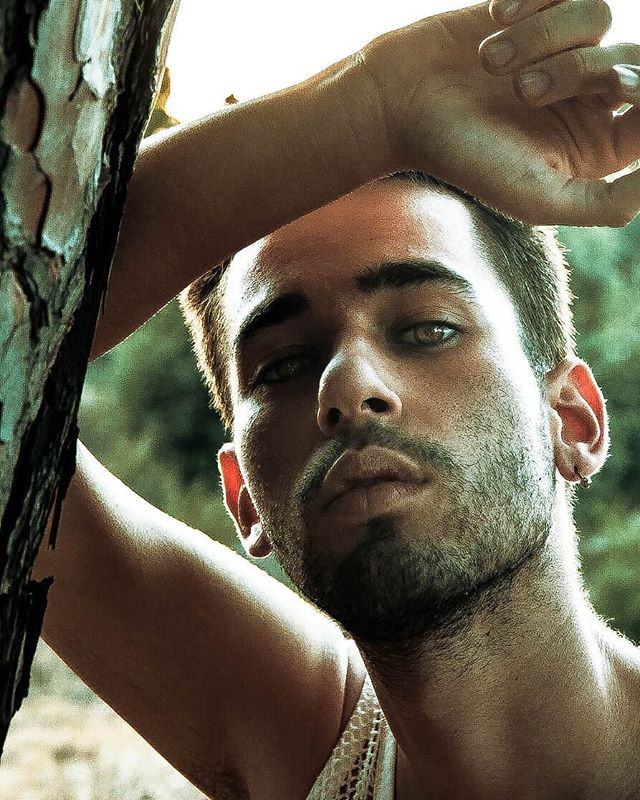 Close up of a handsome man posing near a tree in soft, natural light.