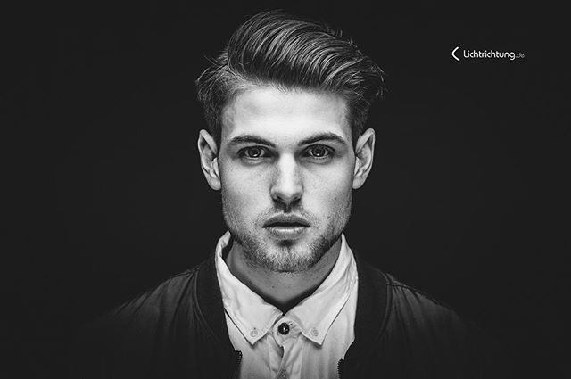 A monochrome portrait of a stylish man with a confident gaze against a dark backdrop.