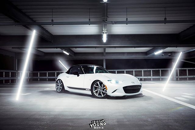 A white Mazda Miata roadster parked in a parking garage under bright artificial lights.
