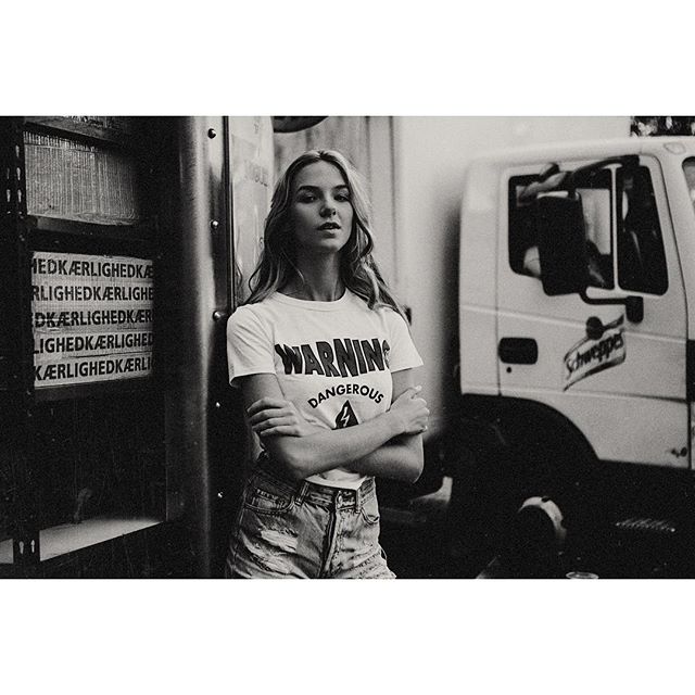 A young woman with blonde hair poses in a black and white urban setting near a truck.