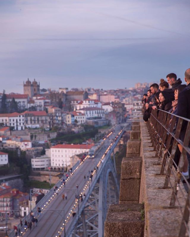 Tourists admire the cityscape from a bridge in Porto, Portugal during a calm evening, showcasing travel and urban beauty.