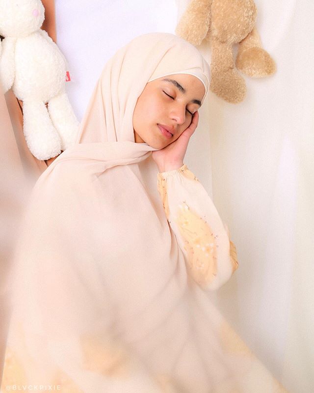 A serene woman wearing a hijab peacefully sleeping indoors.