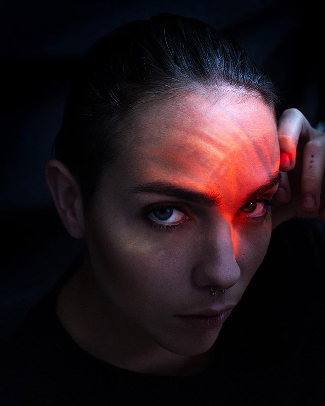 A close-up portrait of a woman with dramatic lighting and red light on her face.