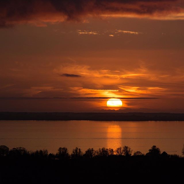 A stunning sunset over a calm lake reflects orange and golden colors in the sky and water.