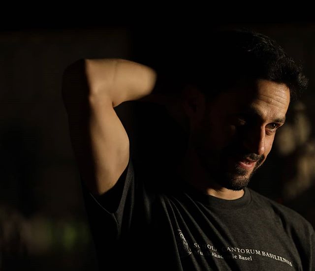 A man with a beard is posing indoors under soft, directional lighting for a portrait.