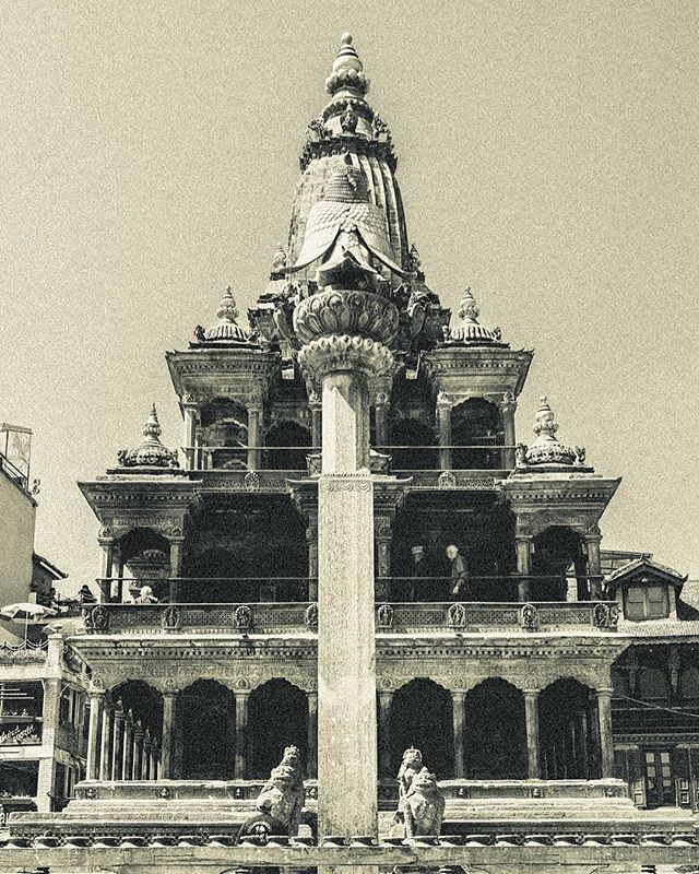 A historic multi-tiered temple with intricate carvings and lion statues stands tall in a sepia-toned scene.