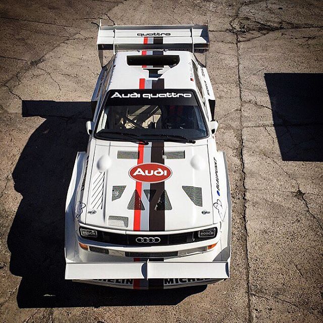 Overhead shot of a white Audi Quattro race car with red and gray stripes parked on concrete.
